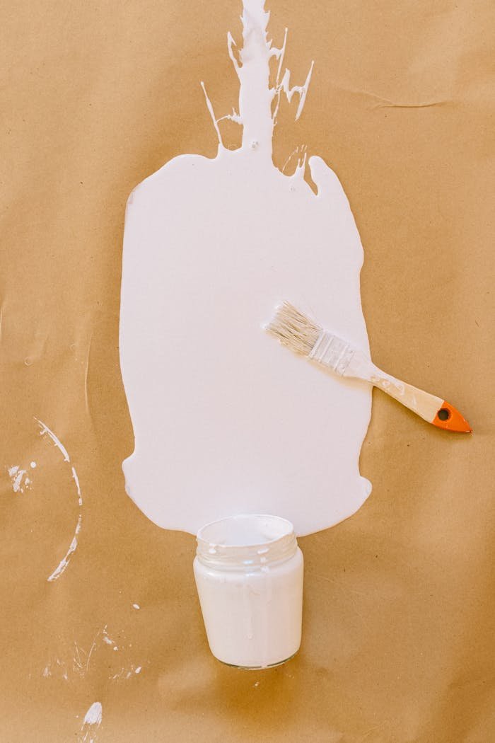 who-we-are A brush beside a white paint spill on brown paper, showcasing a creative art setup.