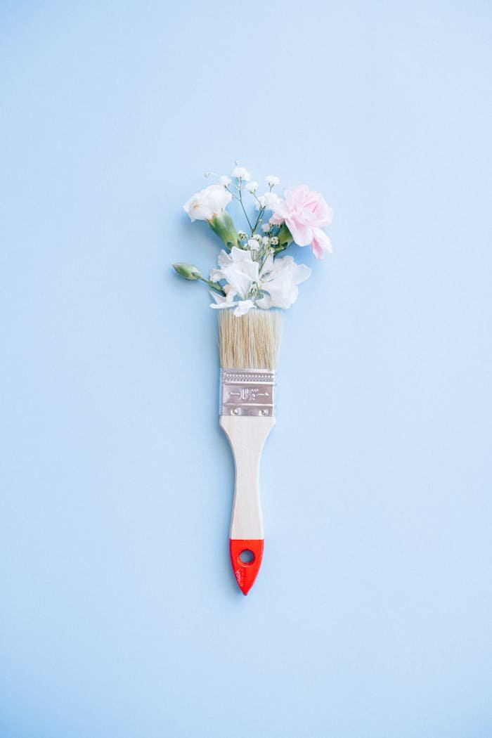 services-02 A minimalist image of a paintbrush adorned with delicate flowers against a blue background.