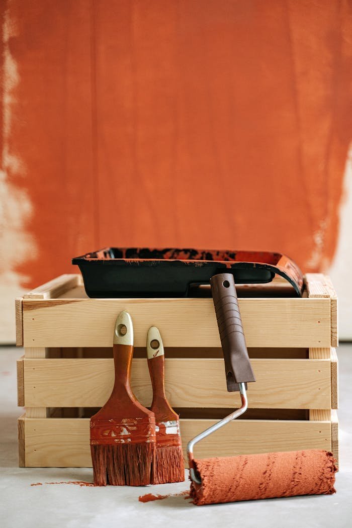 services-04 Wooden crate with paintbrushes and roller against a partially painted wall.