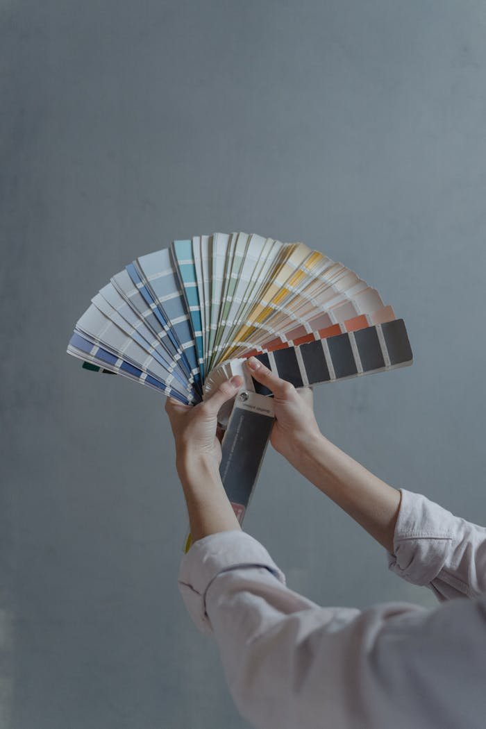our-story Hands displaying a fan of paint color swatches against a gray wall, ideal for home renovation projects.