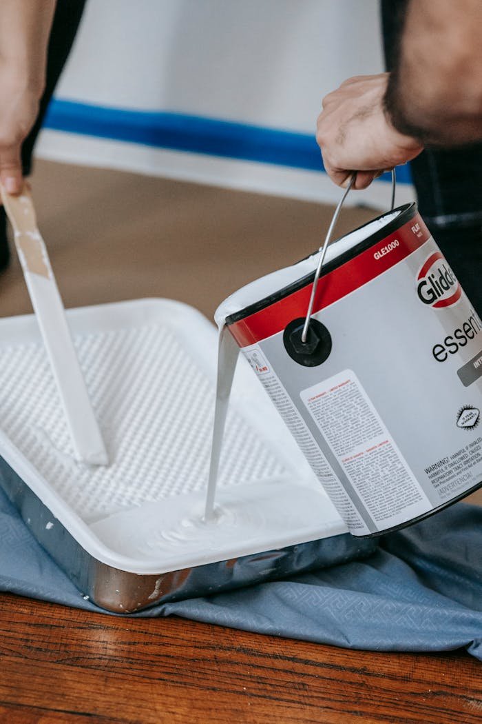 Close-up of white paint being poured into a tray for a home renovation project indoors.